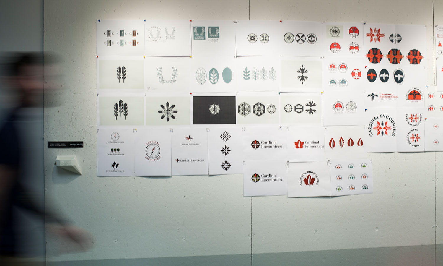 Man walking alongside printouts of logos tacked to wall.