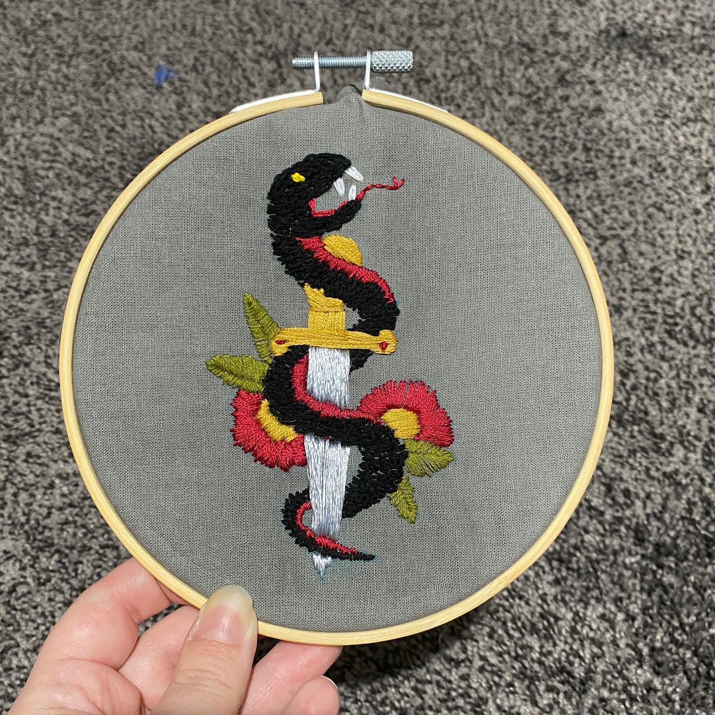 Embroidery of a snake wrapped around a sword with flowers.